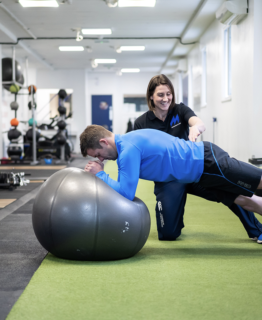 A Momentum staff member helping a client who is doing a plank on an exercise ball